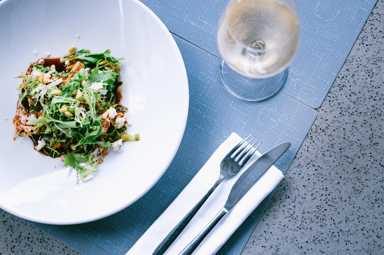 A fresh green salad served with cutlery and a glass of white wine on a set dining table.