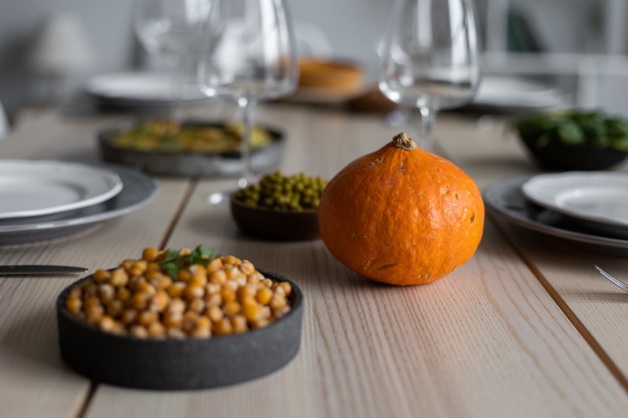 High angle of wooden table served with delicious chickpeas and fresh ripe pumpkin near empty plates and glasses for guests